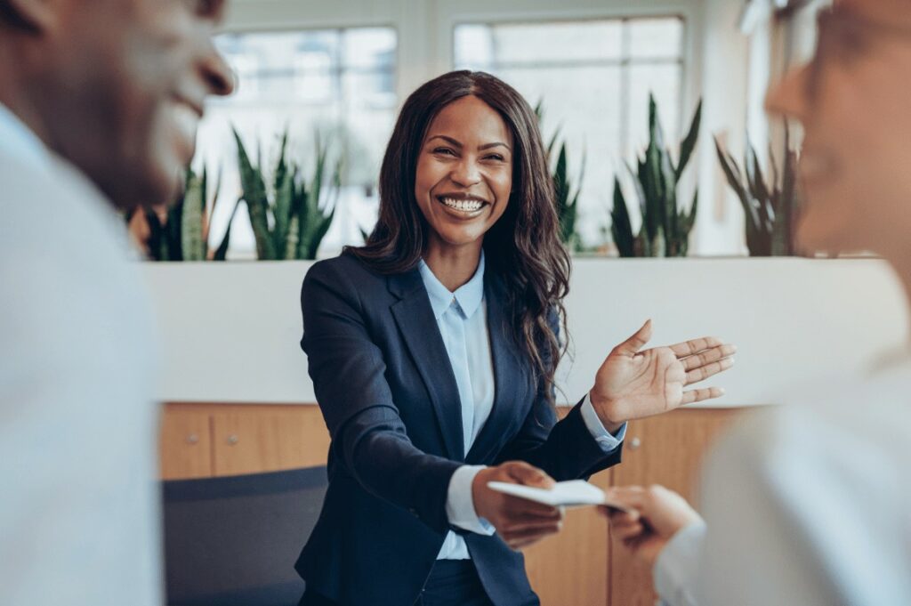 black woman in suit handing a piece of paper to a white woman who smiles and look at african american man